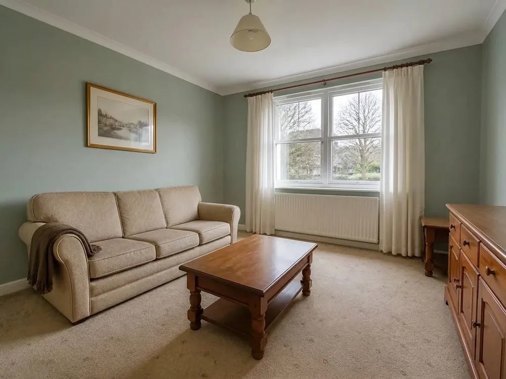Ein Wohnzimmer mit magnolienfarbenen Wänden und derselbe Raum mit salbeigrün gestrichenen Wänden — Sofa, Vorhänge, Fenster und Teppichboden genau dort, wo sie waren — after