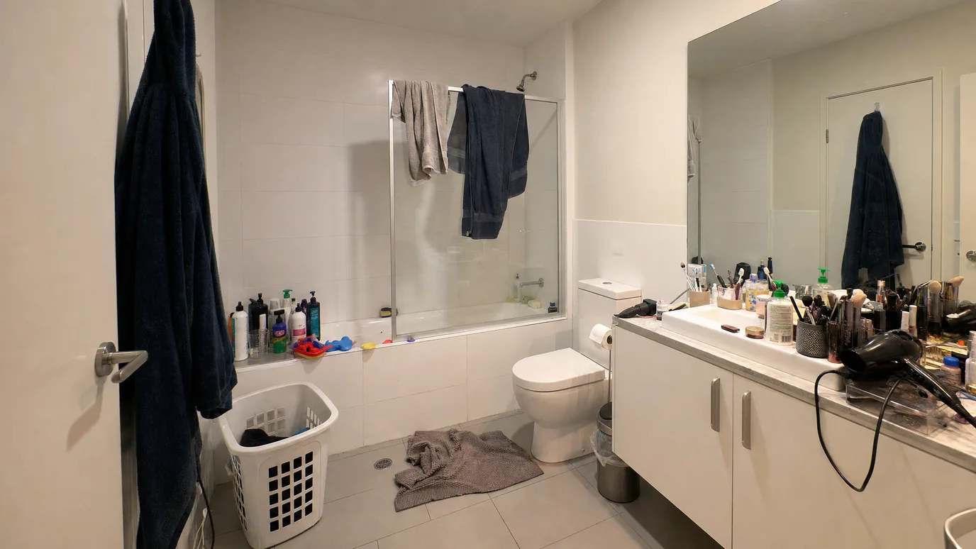 El mismo baño después de despejar — borde de la bañera y lavabo libres, una toalla doblada y los acabados sin cambiar — before